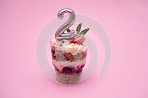Birthday trifle cake with candle labeled number 2 on pink background. portioned mini cake