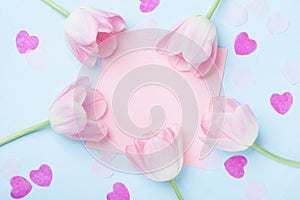 Birthday or wedding mockup with pink paper list, hearts and tulip flowers on blue background top view. Beautiful woman day card.