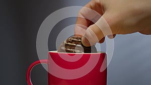 Biscuit dunked into hot drink in a bright red coffee mug