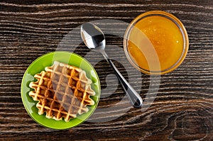 Biscuit waffle in saucer, spoon, transparent bowl with honey on table. Top view