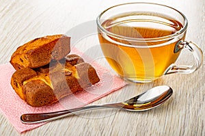 Biscuits with chocolate on pink napkin, transparent cup with tea, spoon on wooden table