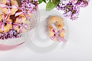 Biscuits with pink ribbon on white plate with lilac flowers, top