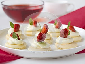 Biscuits with whipped cream, strawsberry, mint on white plate on table against light background