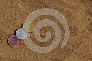Bit coin gold, silver and bronze coin and printed encrypted money, crypt currency concept in a beach sand