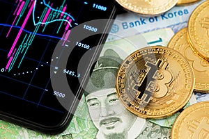 Bitcoin BTC cryptocurrency coins and South Korea Won currency banknotes next to mobile phone.