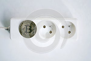 Bitcoin coin lying on power strip extension cord with two empty sockets, cryptocurrency investing, energy consumption footprint