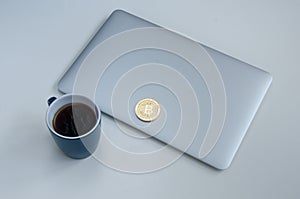 Bitcoin coin near grey laptop and blue coffee cup. Cryptocurrency concept. Isolated on white