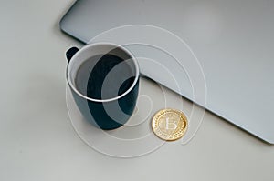 Bitcoin coin near grey laptop and blue coffee cup. Cryptocurrency concept. Isolated on white