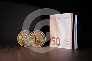 2 Bitcoin coins are next to a bundle of euro banknotes
