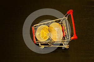 Bitcoin coins in shopping cart. Black background