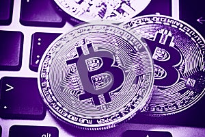 Bitcoin cryptocurrency coins on laptop keyboard. Close up Ultraviolet toned