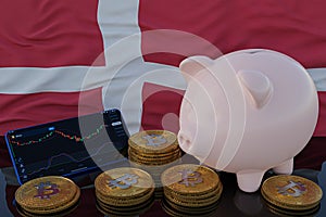 Bitcoin and cryptocurrency investing. Denmark flag in background. Piggy bank, the of saving concept. Mobile application for