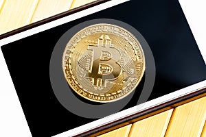 Bitcoin gold coin laying on a smartphone screen, closeup, top view. Golden coin on a mobile phone display, seen from above, app