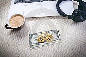 Bitcoin golden coins on a dollar banknotes. Office background. Cup of coffee, white laptop, mobile phone, and money. Money balance