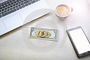 Bitcoin golden coins on a dollar banknotes. Office background. Cup of coffee, white laptop, mobile phone, and money. Money balance
