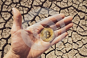 BITCOIN OVER DRY LAND IN HAND SYMBOLIZING GLOBAL WARMING AND CRYPTO MINING