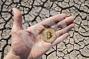 BITCOIN OVER DRY LAND IN HAND SYMBOLIZING GLOBAL WARMING AND CRYPTO MINING