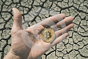 BITCOIN OVER DRY LAND IN HAND SYMBOLIZING GLOBAL WARMING AND CRYPTO MINING