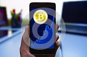 Bitcoin price growth graph. Cryptocurrency Bitcoin symbol and growth chart at the smartphone screen, smartphone in the hand.