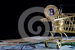 Bitcoins in gold color in a consumer`s basket on a black background. Cryptocurrency, digital money and electronic