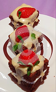 A bites of brownies with stawberries,melted white chocolate ,stuffed with mascarpone on a pastel background.