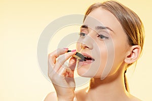 Biting. Close up of beautiful female face with cucumber slice over yellow background. Cosmetics and makeup, natural and