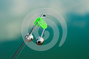 Biting indicator, nod, in the form of bells on the tip of the rod against the background of the reflection of the sky in the water