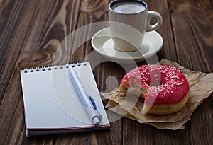 Bitten donut cup of coffee and notebook