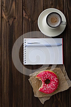 Bitten donut cup of coffee and notebook