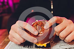 A bitten fresh burger in the hands of a man.
