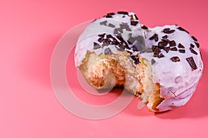 Bitten glazed donut with chocolate chip on top isolated on a pink background
