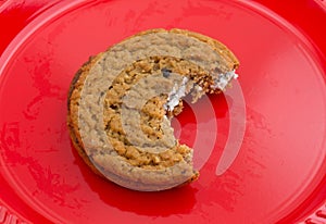 Bitten oatmeal crÃ¨me cookie on a red plate