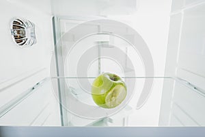 Bitten off green apple on shelf of refrigerator with open door