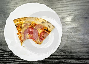 A bitten portion of pepperoni pizza on a plate. View from above.