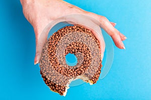 Bitten tasty chocolate donut with sprinkle in woman`s hands