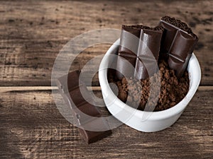 Bitter aerated chocolate bars and cocoa powder in white bowl on the wooden table. Pieces of dark porous chocolate