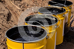 Bitumen mastic in buckets. Protective bitumen mastic for concrete pavement. Material for waterproofing the foundation