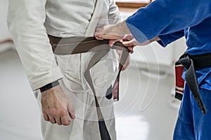 BJJ brazilian jui jutsu belt promotion close up on hands of unknown instructor black belt professor tie up brown belt on waist of photo