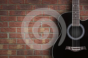 Black acoustic guitar on brick background with copy space
