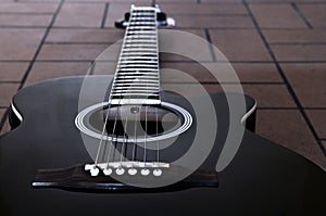 Black acoustic guitar on the brick floor. Closeup top-down photo.