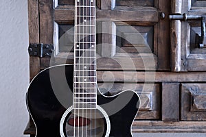 Black acoustic guitar in front of vintage wooden cupboard.