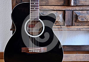 Black acoustic guitar in front of vintage wooden cupboard.