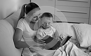 Black adn white portrait of mother with baby lying in bed and reading book