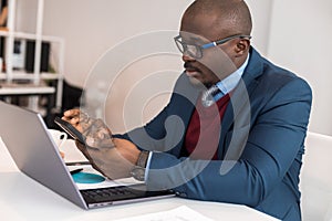 A black African American businessman in a business suit works at a laptop. Self-development and distance learning