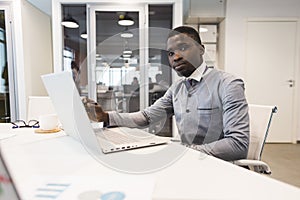 A black African American businessman in a national ethnic business suit works at a laptop. Analytics and work online