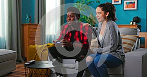 Black African-American excited man sitting on a sofa, holding a joystick playing video games, feeling