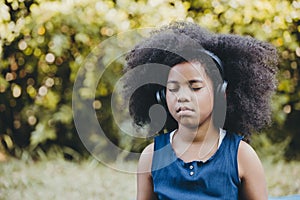 Black african girl children using headphones listening music eyes closed focus and concentrate at green park outdoor photo