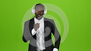 Black african guy listens to music through headphones and sings along. Green screen