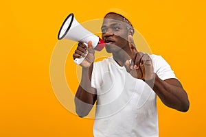 Black african man speaks in megaphone on isolated yellow background