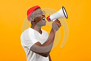 Black african man speaks in megaphone on isolated yellow background photo